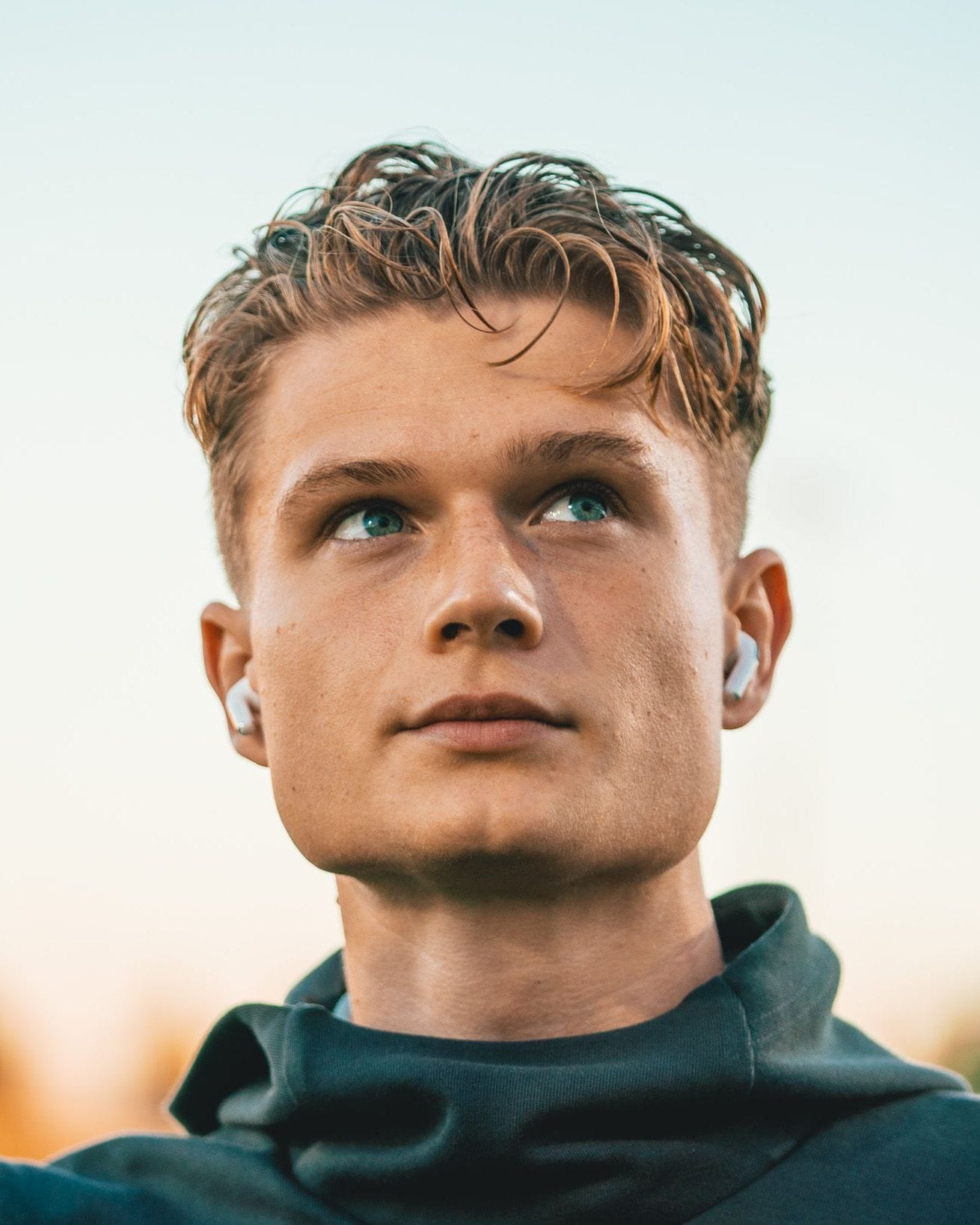 Erik McCue in a dark hoodie, looking up and to the side against a soft evening sky.